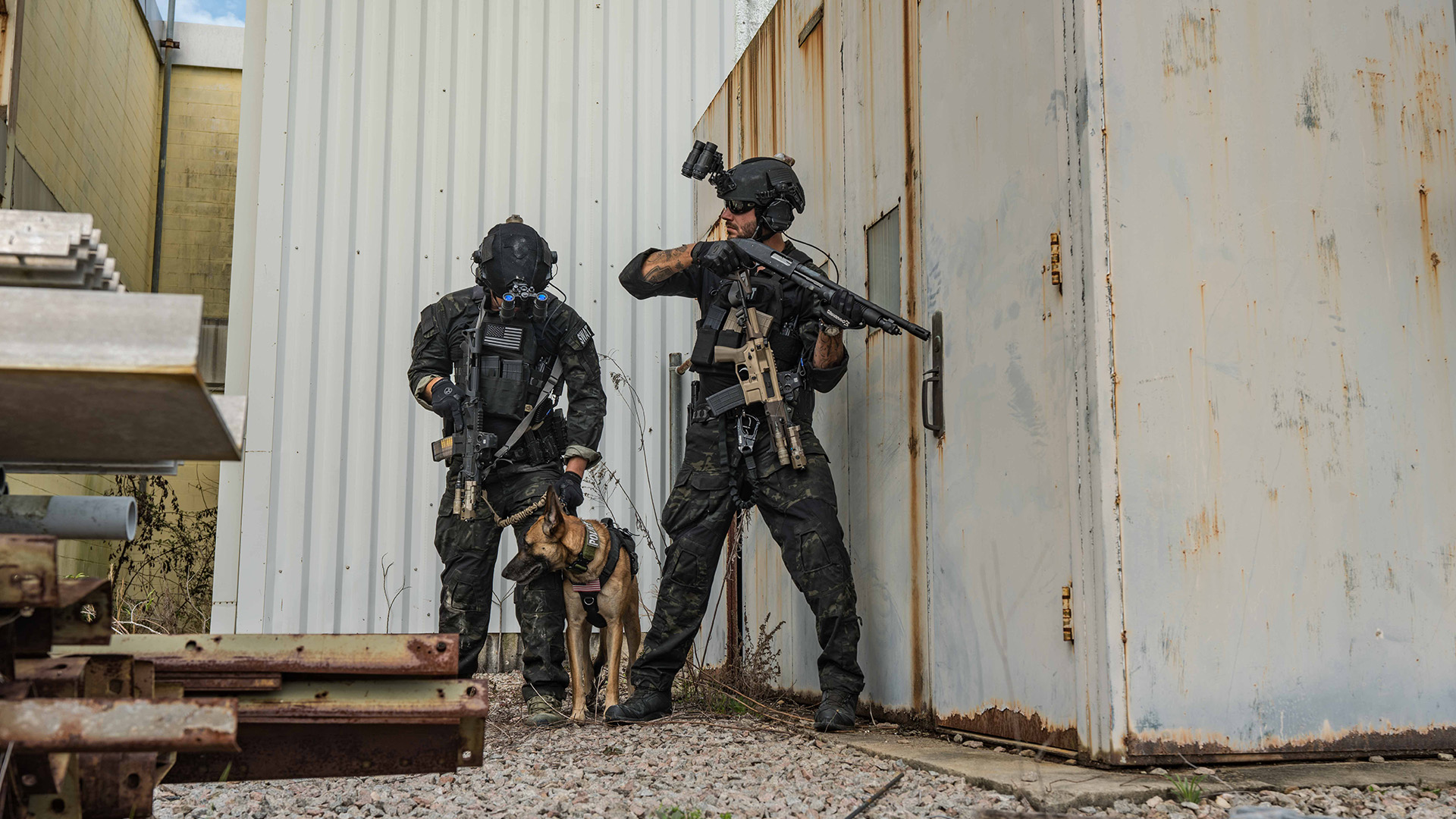 Two men in army camo with a dog holding guns