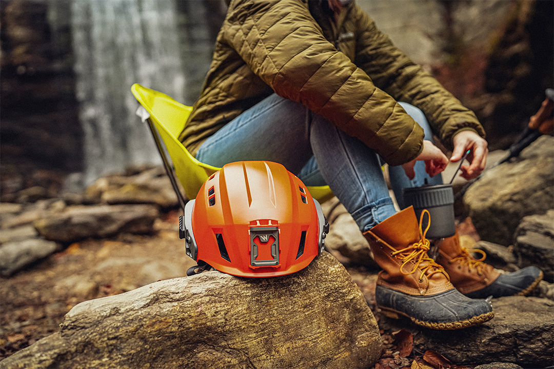 Image of orange helmet on log next to the legs of a person out of image
