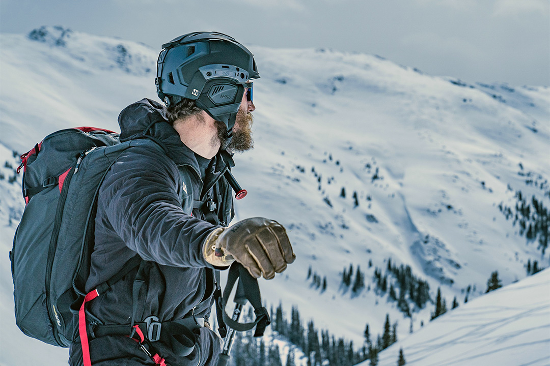 Snow covered mountain range and man in backpack, helmet and coat